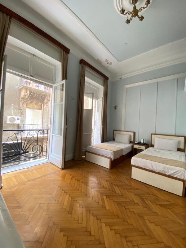Twin Room private balcony at Sufi House Hostel with two chairs and a table, offering a clear view of Downtown Cairo buildings.