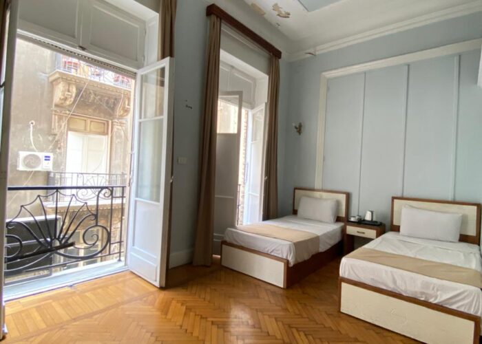 Twin Room private balcony at Sufi House Hostel with two chairs and a table, offering a clear view of Downtown Cairo buildings.