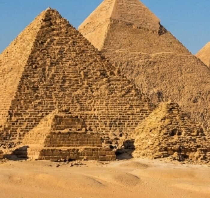 The three Giza pyramids rising above the desert sand under a clear blue sky