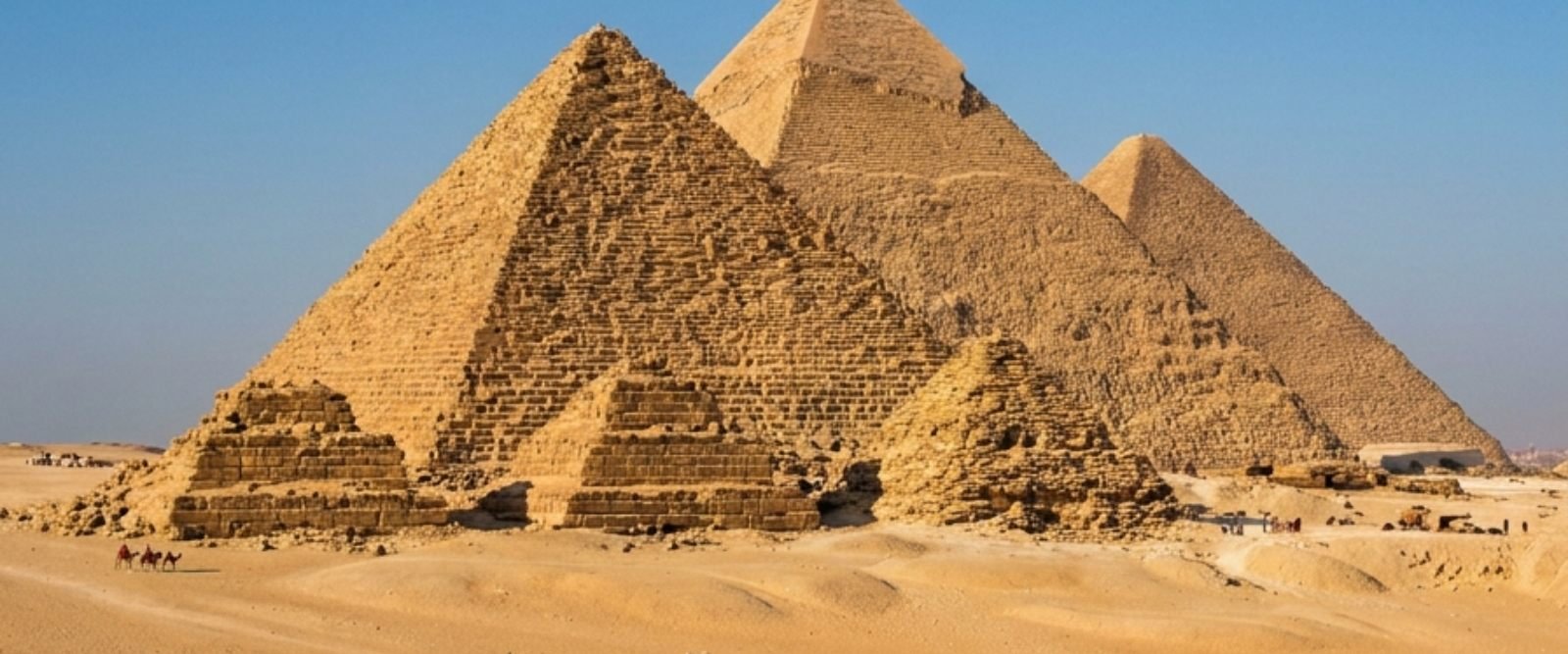 The three Giza pyramids rising above the desert sand under a clear blue sky
