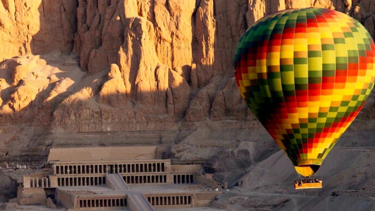 Hot air balloon drifting past Hatshepsut Temple and the Theban cliffs at sunrise, Luxor West Bank